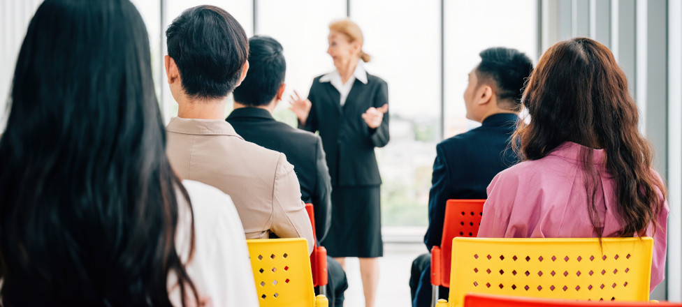 A confident senior corporate coach leads a seminar for a business team. The female director, CEO, and employees actively participate in an office meeting, discussing projects and guiding.